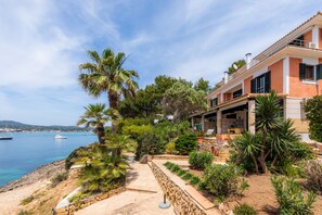 A coastal property with a stone pathway, palm trees, and a view of the sea. - Holiday Home Es Niu with Sea View, Garden and Wi-Fi (Portocolom)