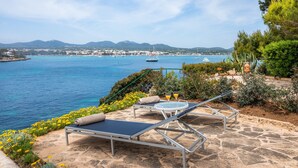 A seaside terrace with lounge chairs, a table, and a drink. - Holiday Home Es Niu with Sea View, Garden and Wi-Fi (Portocolom)