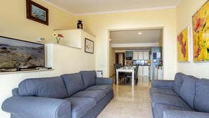 A living room with two grey sofas, a flat-screen TV, a painting, and a kitchen in the background. - Holiday Apartment 'Daniela' next to the Beach with Sea View, A/C, Balcony & Wi-Fi (Pollenca)