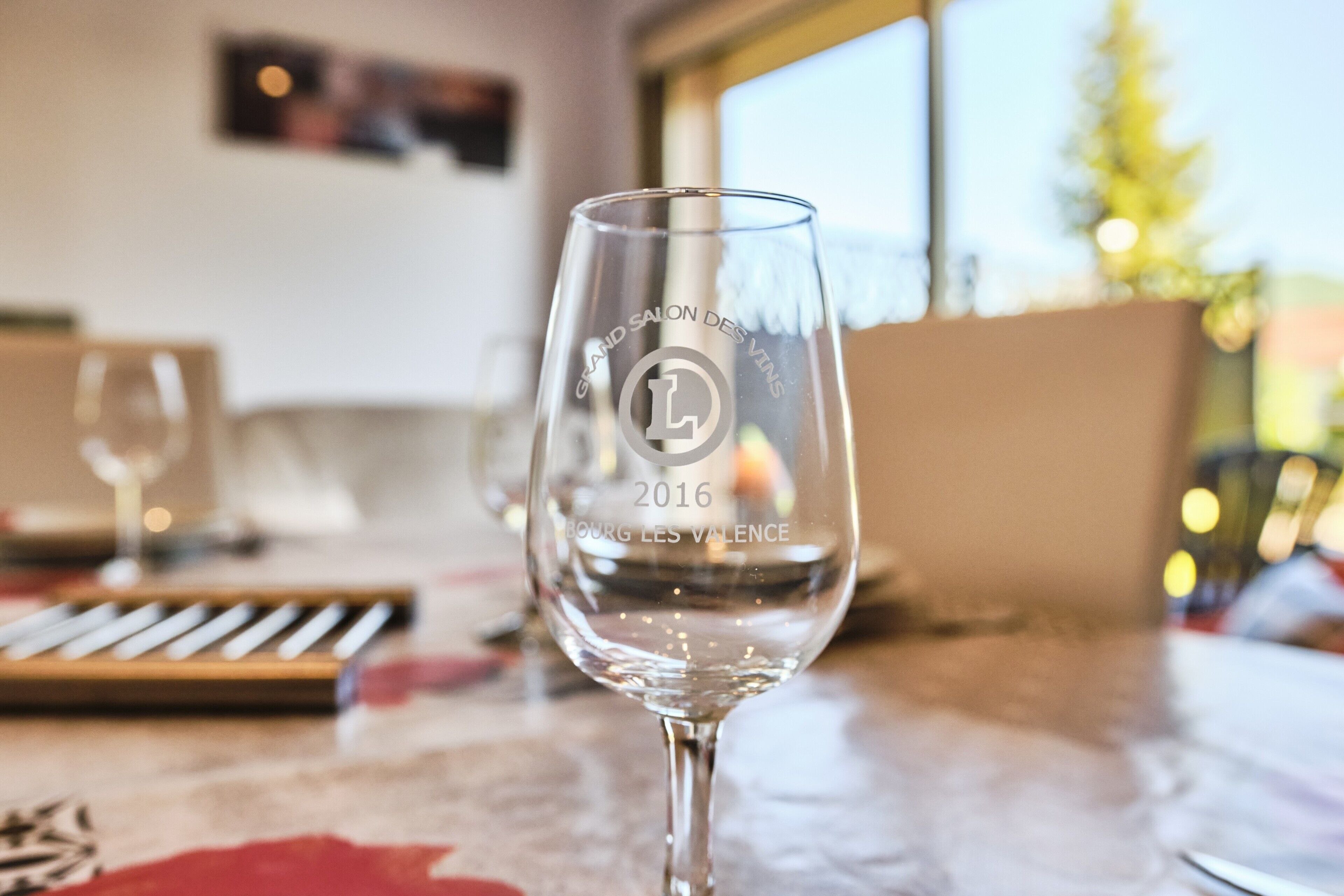 A clear glass with embossed text and a year, placed on a table with a patterned tablecloth.