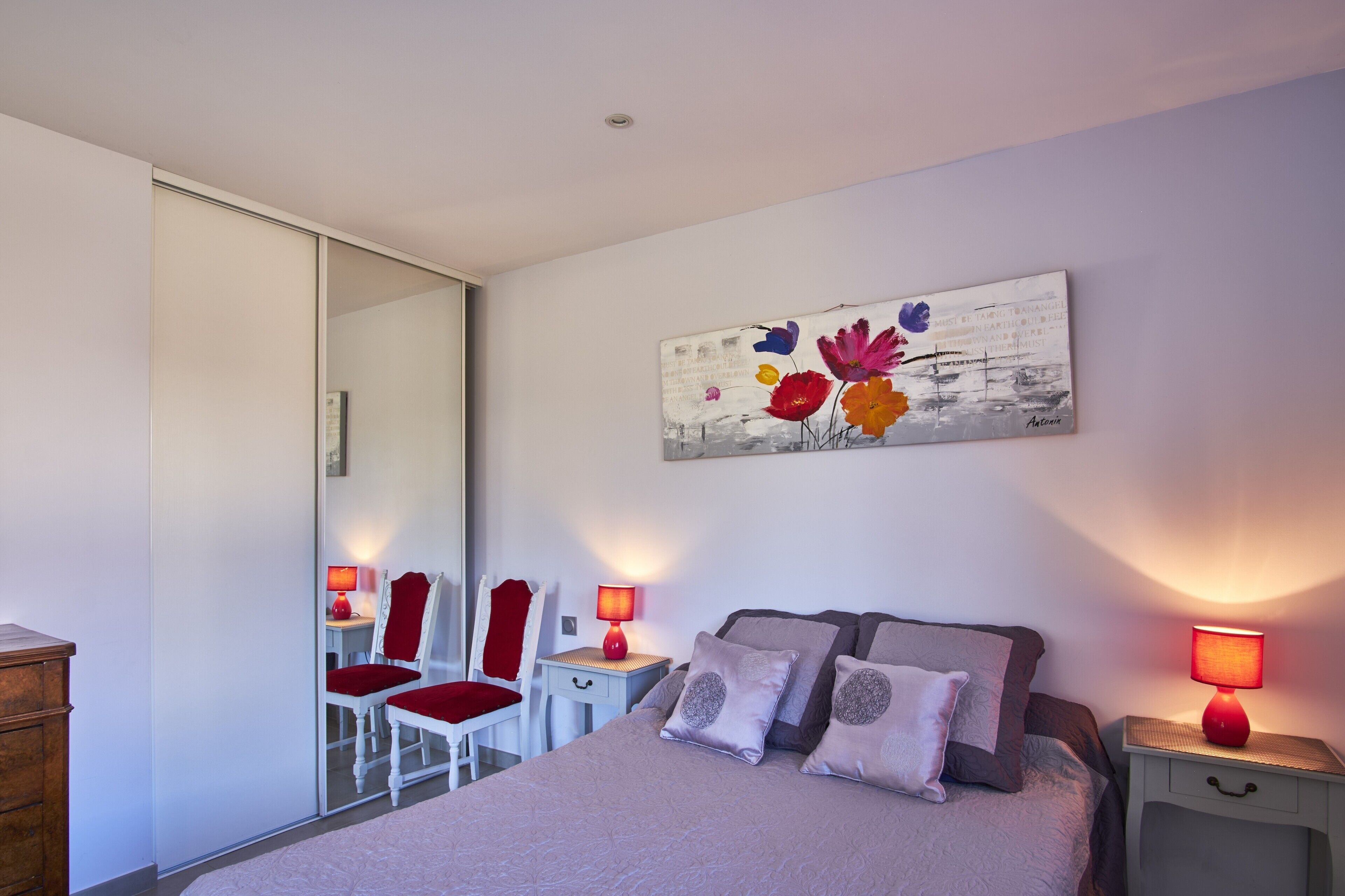 A bedroom with a bed, two bedside tables with lamps, a chair, a dresser, and a mirror.