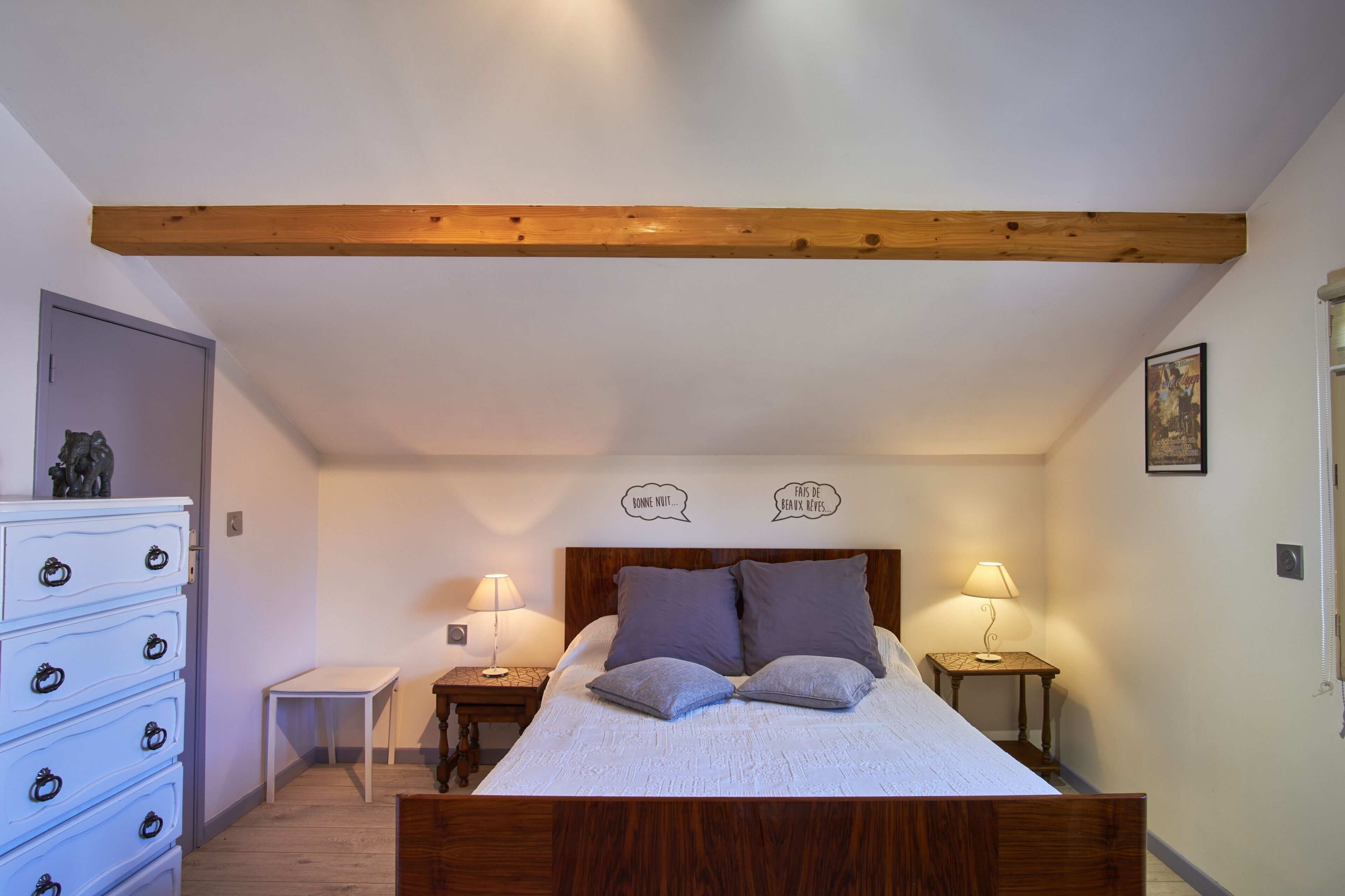 Un dormitorio con techo de madera, una cama con almohadas, un aparador y dos lámparas de noche.