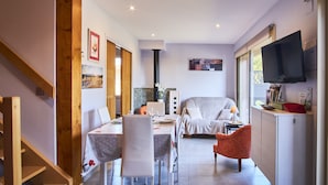 A dining area with a table set for four, a sofa, a TV mounted on the wall, and a staircase.