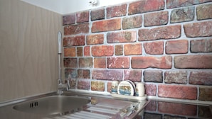 Una cocina con un lavamanos de acero inoxidable, salpicadero de azulejos y encimera con una tetera y un juego de platos pequeño.
