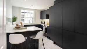 A modern kitchen with a white countertop, dark cabinetry, and a window providing natural light.