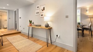 A modern living room with a wooden floor, a rug, a console table with a lamp, and framed pictures on the wall.