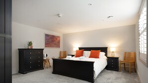 A bedroom with a large bed, two bedside tables, a dresser, a chair, and a wall-mounted shelf.