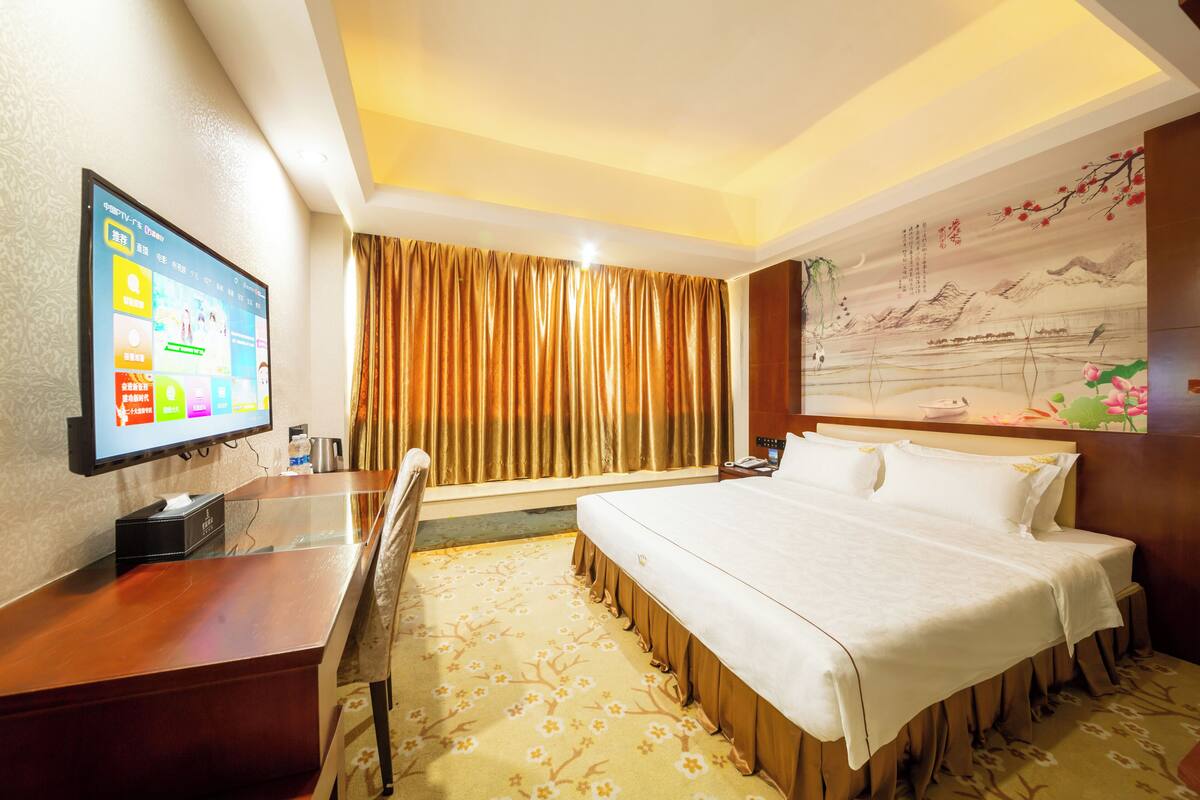 A hotel room with a bed, a desk, a television, and a large window with curtains.