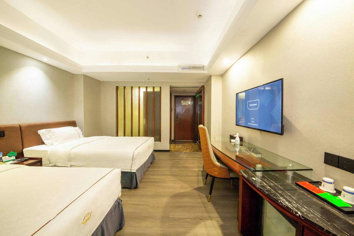 A hotel room with two beds, a desk, a chair, a TV, and a bathroom door.