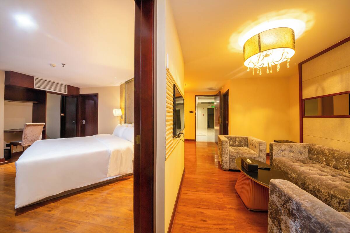 A hotel room with a bed, a desk, a chair, a sofa, and a TV.