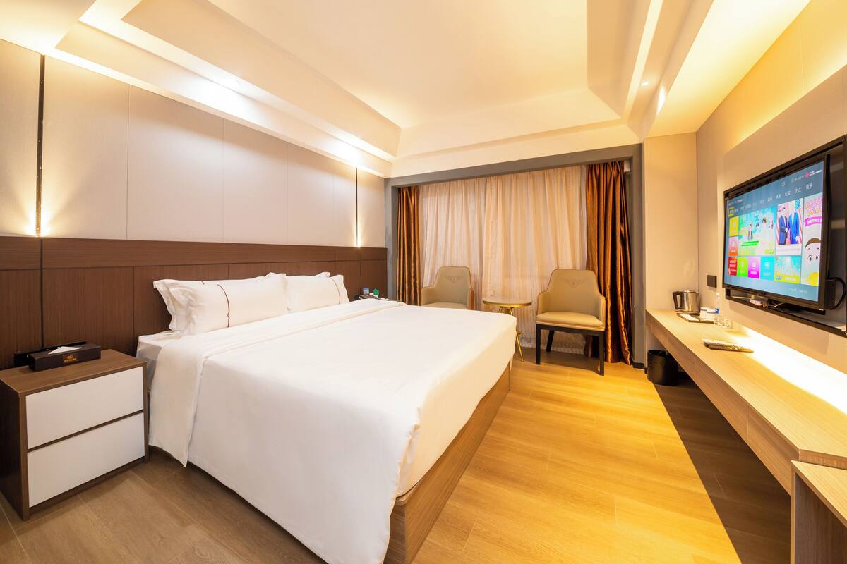 A hotel room with a large bed, a desk with a TV, and a chair.