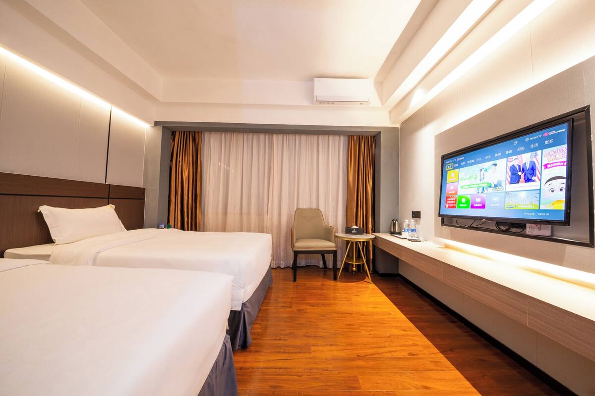 A hotel room with two beds, a TV, a desk, and a chair.