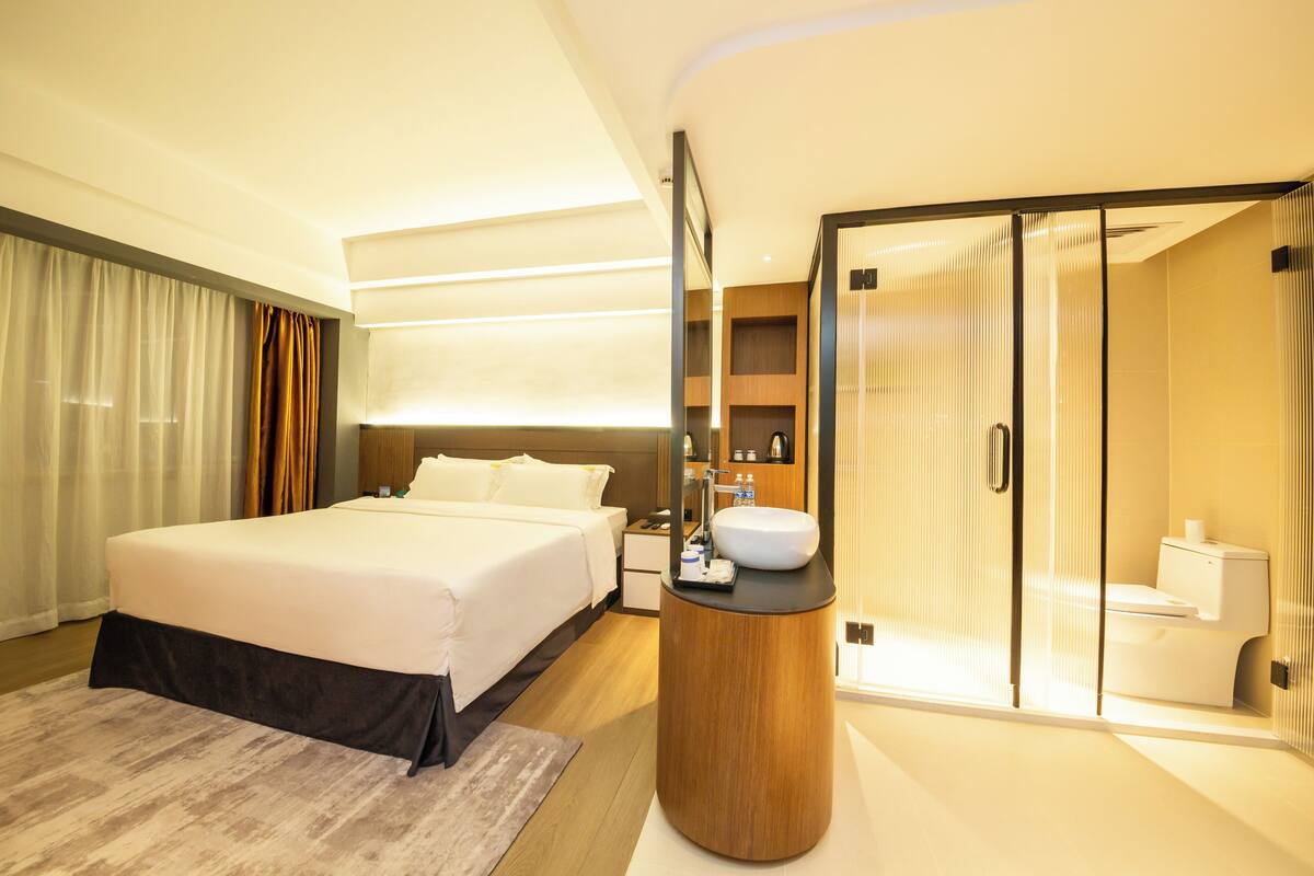 A modern hotel room with a large bed, a round vanity with a sink, and a separate shower area.
