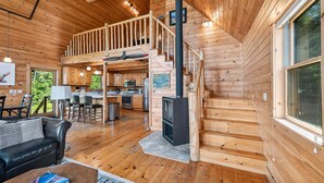 A cabin interior with a wooden staircase, a kitchen area, and a living room with a sofa and a coffee table. - Alpenglow - 3 bedroom, 2 bath home on Haley Pond (Rangeley)