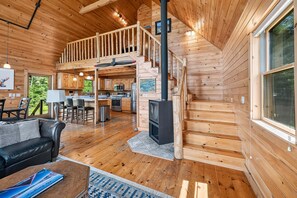A cabin interior with a wooden staircase, a kitchen area, and a living room with a sofa and a coffee table.