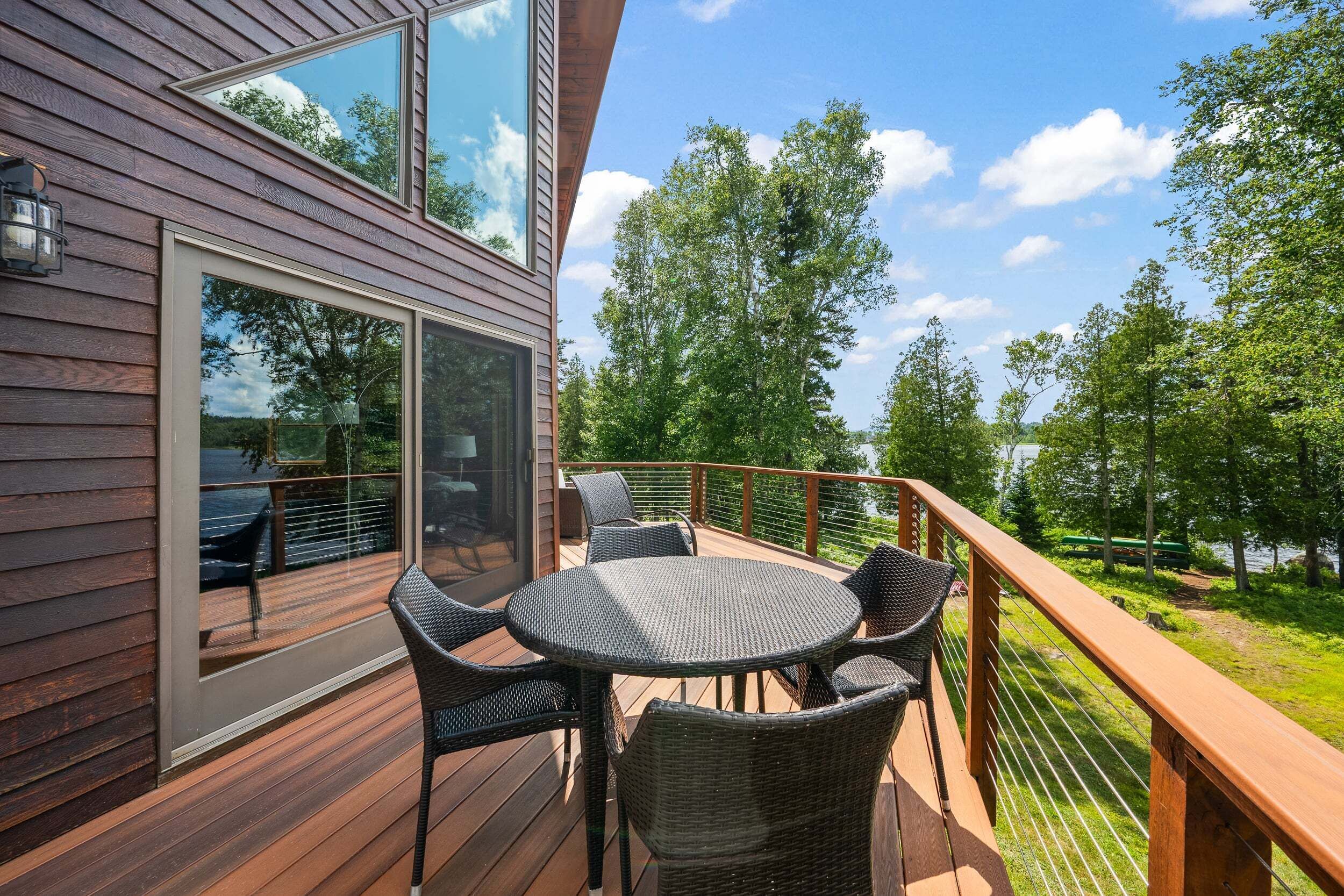 Una terraza con mesa y sillas, con vista a un lago rodeado de árboles.