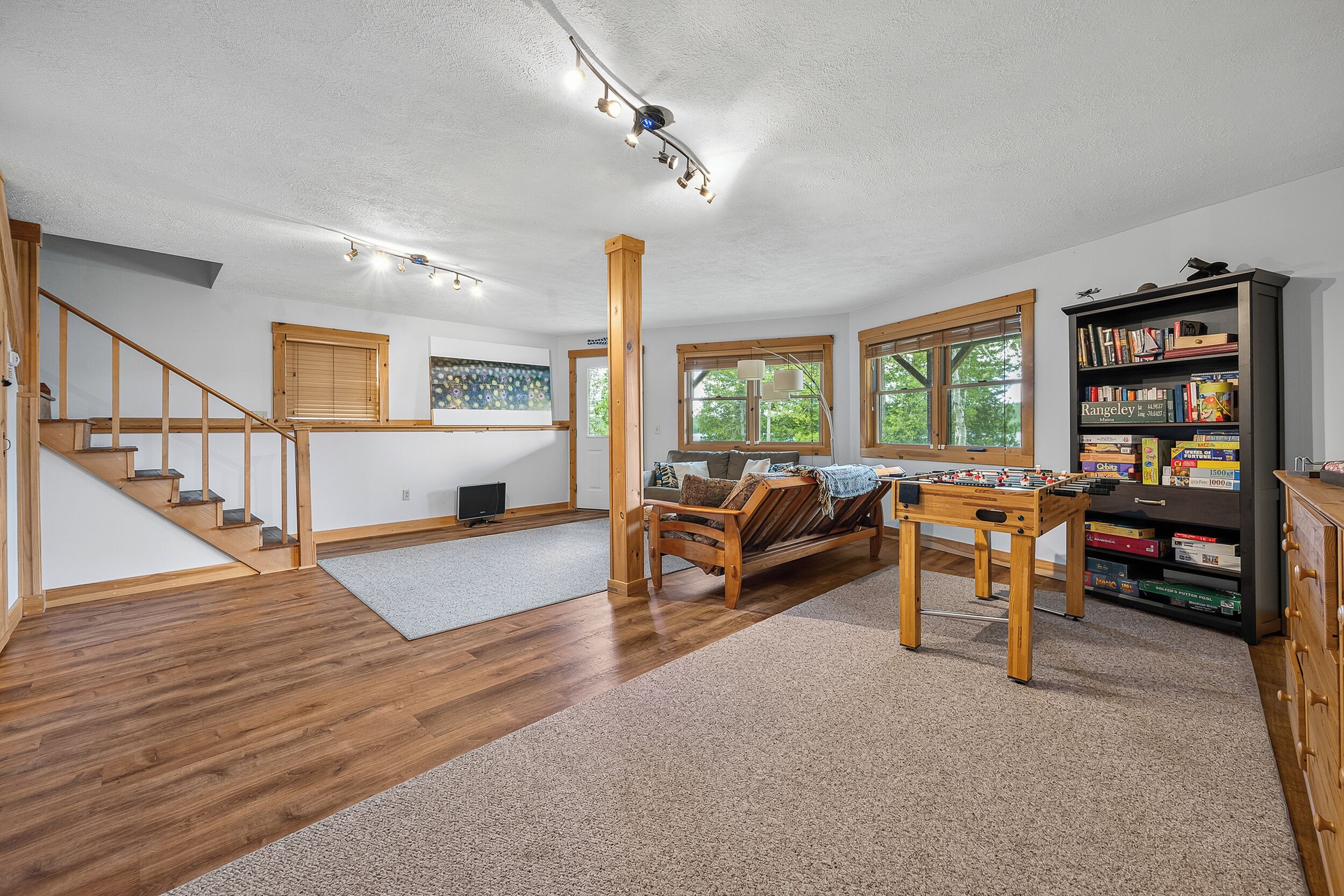 A spacious room with a wooden staircase, a foosball table, and a bookshelf filled with board games.