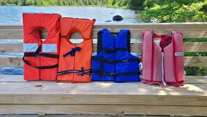 Life jackets on a wooden bench by a lake.