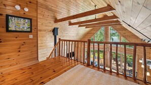 A wooden interior with a staircase leading to an upper level, a framed painting on the wall, and a view of greenery outside. - Alpenglow - 3 bedroom, 2 bath home on Haley Pond (Rangeley)