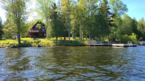 A lakeside cabin with a dock and a small pier, surrounded by lush greenery and trees.