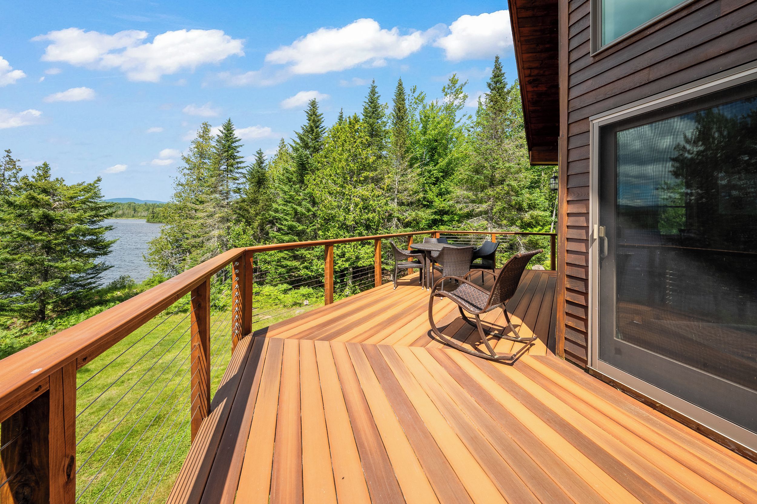Eine Holzterrasse mit Glastür, mit Blick auf einen See und Wald.
