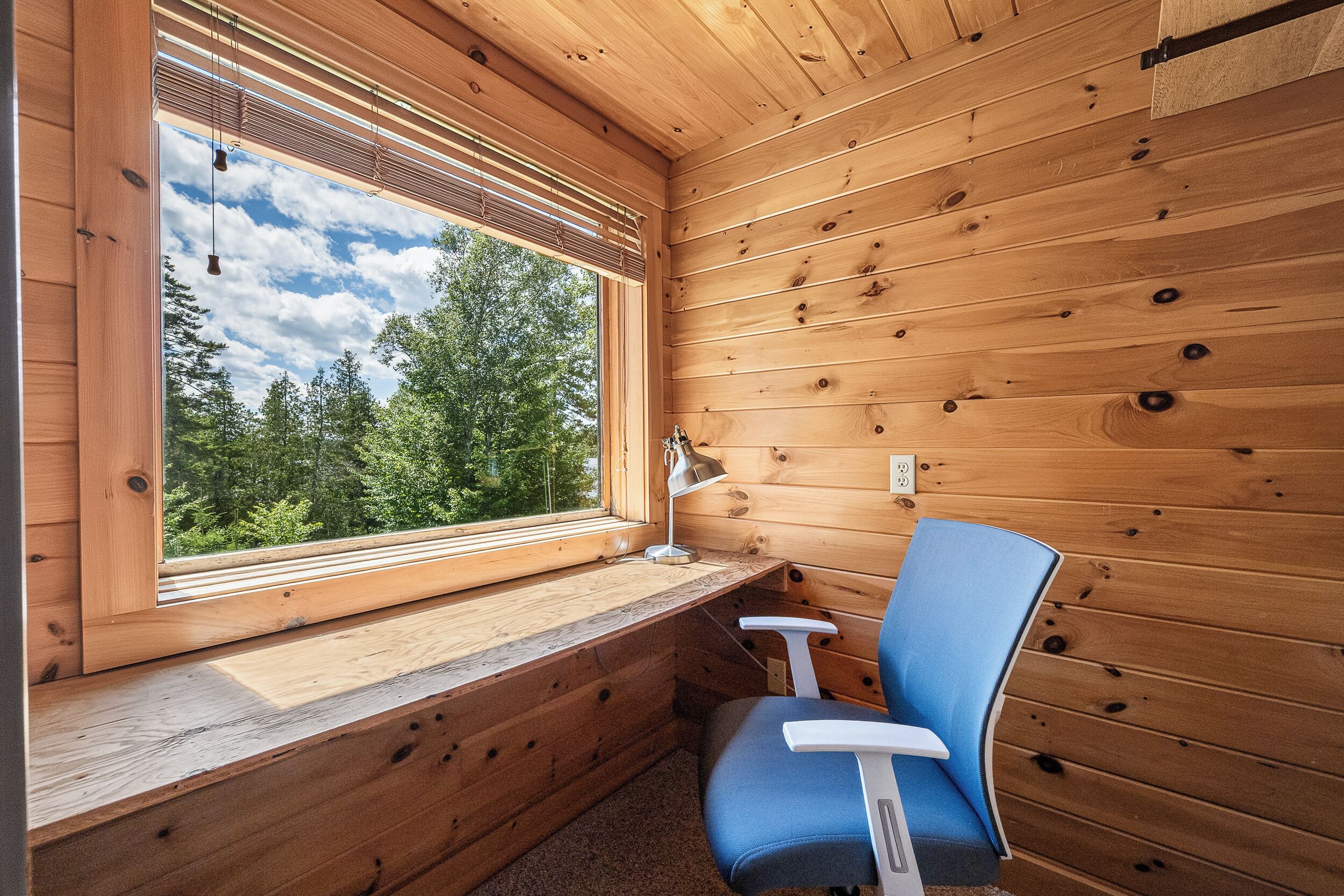Ein Holzblockhaus-Interieur mit einem großen Fenster, einem Schreibtisch und einem blauen Stuhl.
