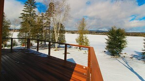 A wooden deck with a view of a snowy landscape and trees. - Alpenglow - 3 bedroom, 2 bath home on Haley Pond (Rangeley)