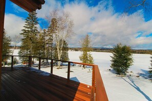 A wooden deck with a view of a snowy landscape and trees.
