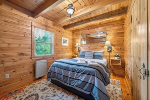 Een slaapkamer in een houten hutje met een bed, nachtlampjes, een raam en een radiator.