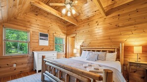 A wooden cabin bedroom with a bed, bedside table, lamp, and a view of the forest through the window. - Alpenglow - 3 bedroom, 2 bath home on Haley Pond (Rangeley)