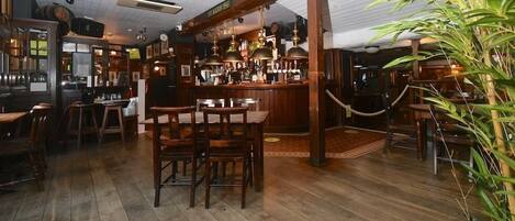 A bar area with wooden furniture, a bar counter, and hanging light fixtures.