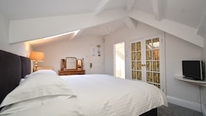 Een slaapkamer met een groot bed, een nachtkastje met een lamp, een televisie op een meubel en een deur met raam.