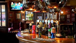 Een bar met een gepolijst bargedeelte, meerdere tappunten en een televisie op de achtergrond.