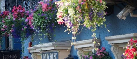 Facciata di un edificio con cesti di fiori pensili e un'insegna con la scritta 'TENNY HOUSE'.