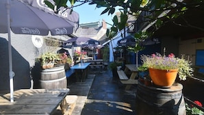 Een terras met tafels en banken, omringd door potplanten en parasols.