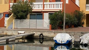 A residential building with a red facade, white balconies, and a small boat docked in the water. - 5-Bedroom Marina with A/C, Pool, Private Pontoon, Sleeps 8 - Port Barcarès (Le Barcarès)