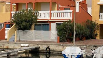 Un immeuble résidentiel à la façade rouge, doté de balcons blancs, et sur lequel on peut apercevoir un petit bateau amarré dans l’eau.