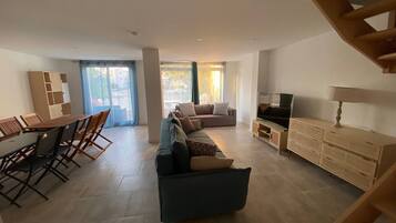 Un grand espace de vie comprenant un canapé, un téléviseur et un coin repas avec des chaises et une table.