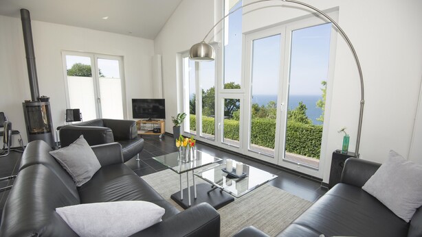 Ett modernt vardagsrum med en svart lädersoffa, ett soffbord i glas och ett stort fönster med utsikt över havet.