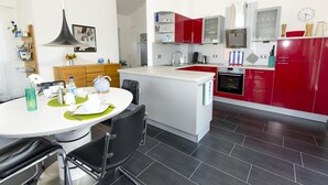 Ett modernt kök med röda skåp, en vit bänkskiva och en matplats med ett vitt bord och svarta stolar.