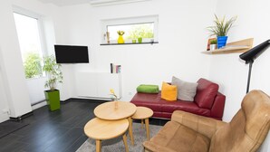 Un soggiorno moderno con un divano in pelle rossa, due tavolini in legno, una TV a parete e una finestra con piante in vaso.