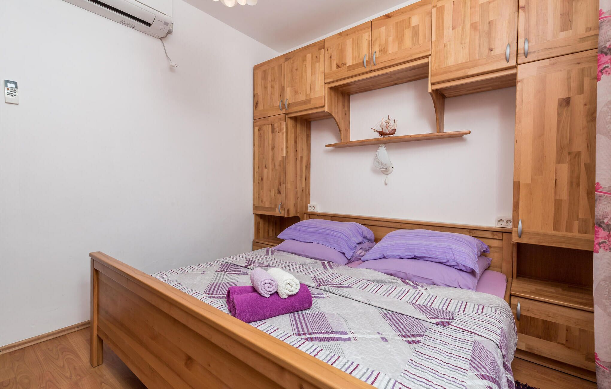 Een slaapkamer met een houten bed, paars beddengoed en een klein plankje met een decoratief object.