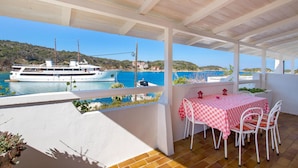 A covered outdoor seating area with a table and chairs, overlooking a body of water with a boat and a hilly landscape. - Awesome apartment in Supetarska Draga with WiFi (Supetarska Draga)