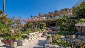 A Mediterranean-style villa with a stone pathway leading to the entrance, surrounded by lush gardens and flowering plants. - Awesome apartment in Supetarska Draga with WiFi (Supetarska Draga)