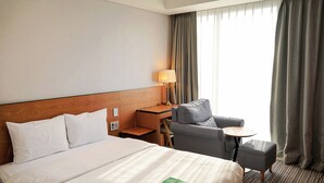 A hotel room with a large bed, a desk, a chair, a small table, and a view of the outdoors. - Hotel Tour (Incheon)