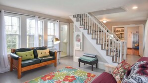 A living room with a wooden sofa, a colorful rug, a staircase, and a kitchen in the background. - Walk to Restaurants Shopping & Harbor! (Wellfleet)