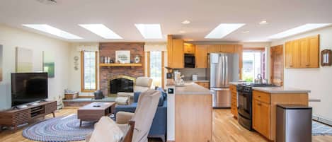 Ein geräumiges Wohnzimmer mit großem Fernseher, Kamin und einer gemütlichen Sitzecke. Die Küche verfügt über Holzschränke und moderne Geräte.