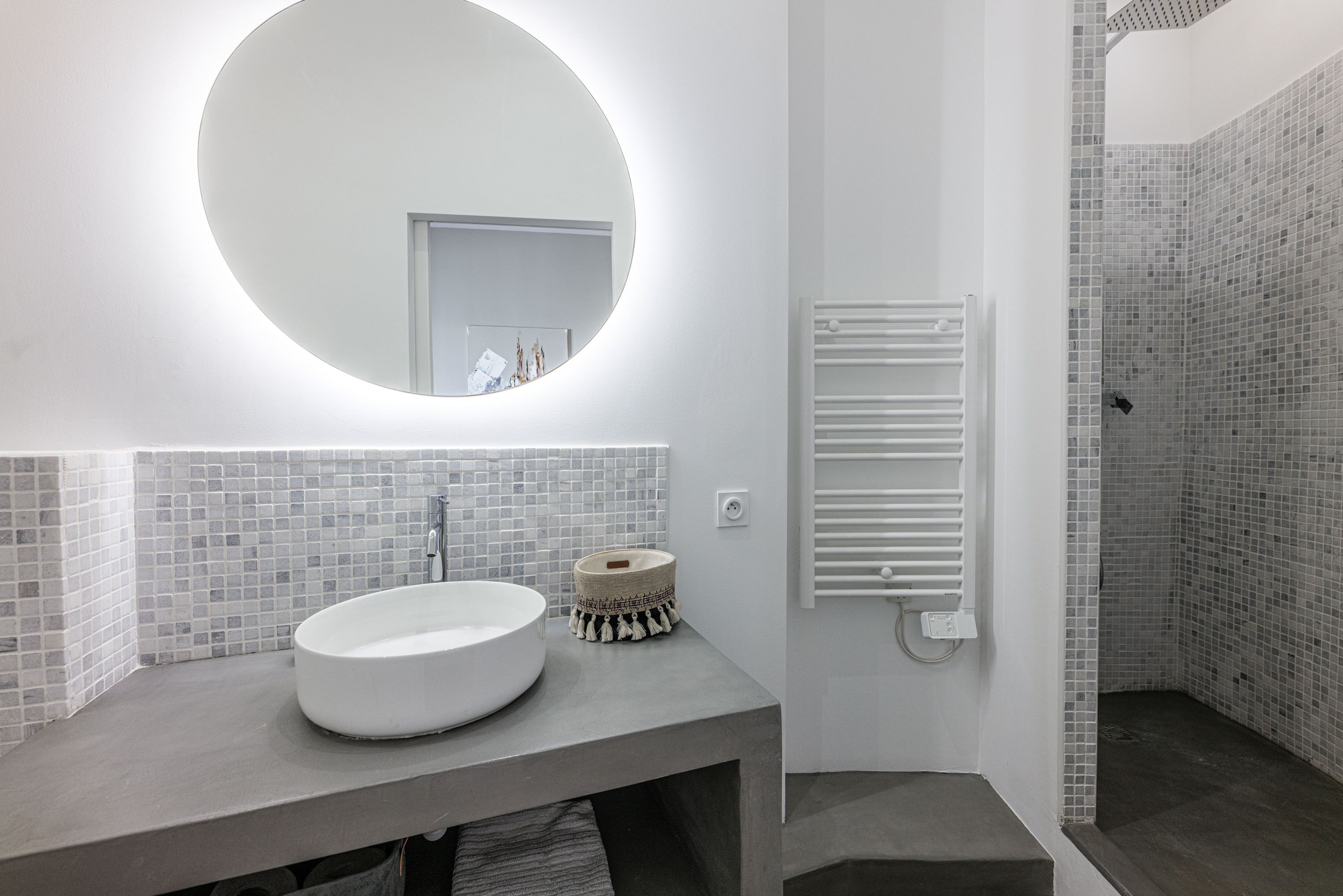 A modern bathroom with a round mirror, a white sink, and a tiled shower area.