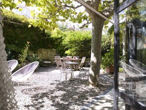 An outdoor patio with a table and chairs, surrounded by greenery and a stone wall. - By the sea, a magnificent 150-square-meter apartment with a garden (Marseille)