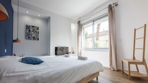 A bedroom with a large bed, a window with curtains, a wooden chair, and a painting on the wall. - Seaside, magnificent 150m2 apartment with garden (Marseille)